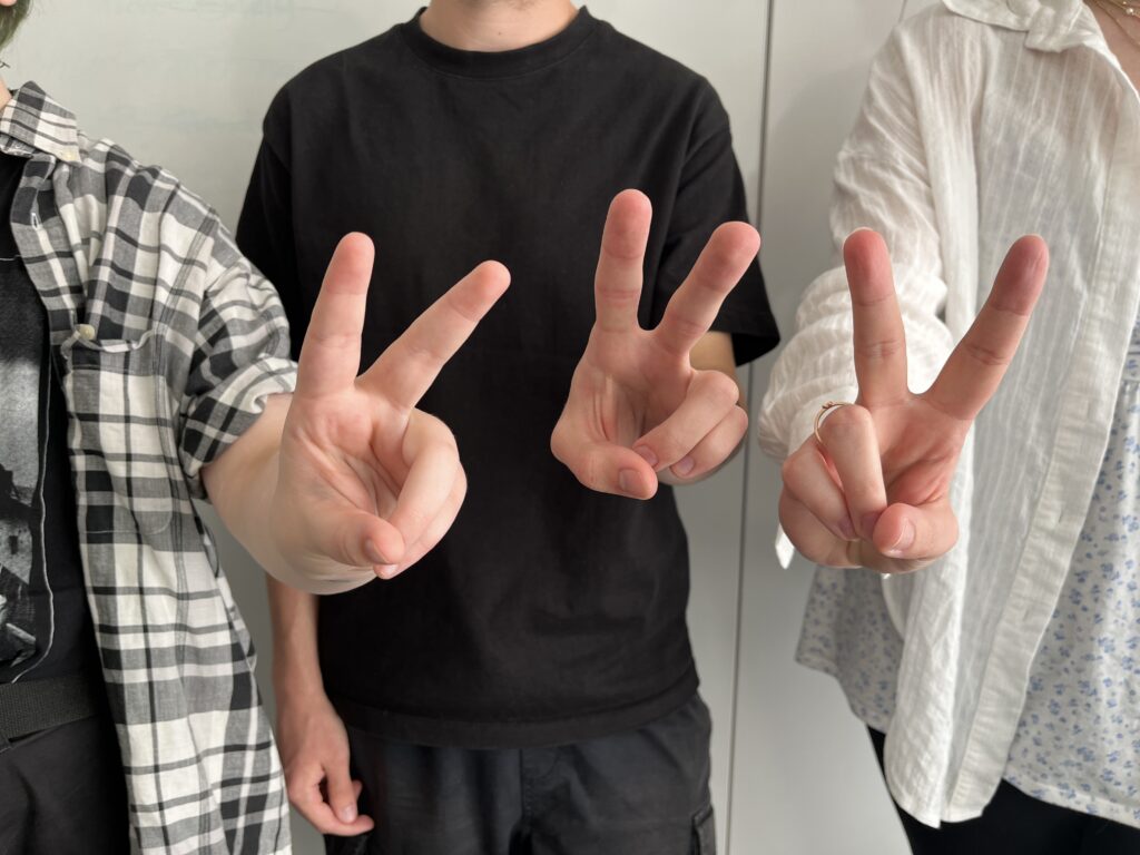 3 junge Leute zeigen vor Freude mit ihren Fingern das Freiheitszeichen