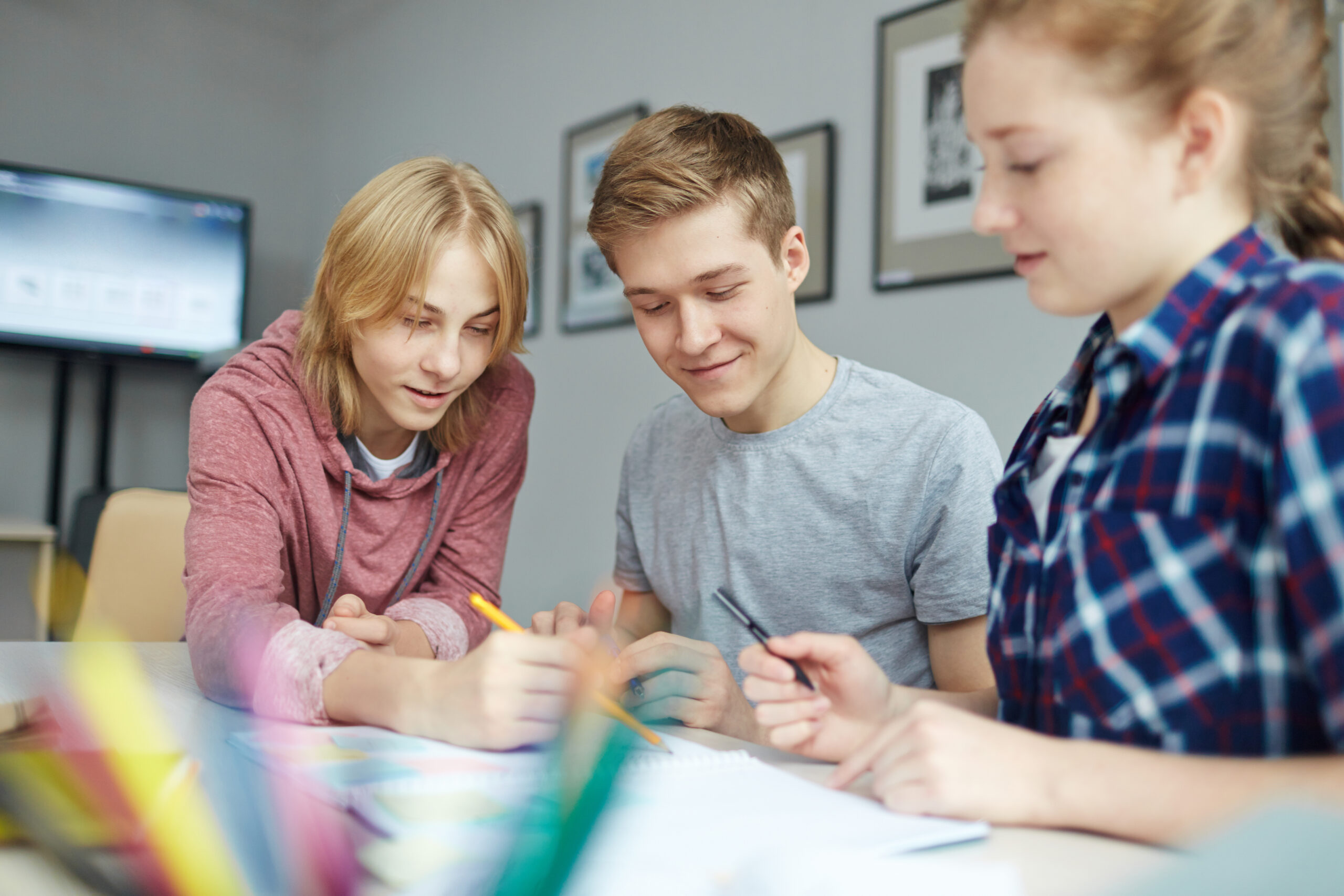 Drei junge Menschen sitzen zusammen an einem Tisch und lernen gemeinsam. Sie haben freudige Gesichter. Es macht ihnen Spaß zusammen zu sitzen und zu reden.